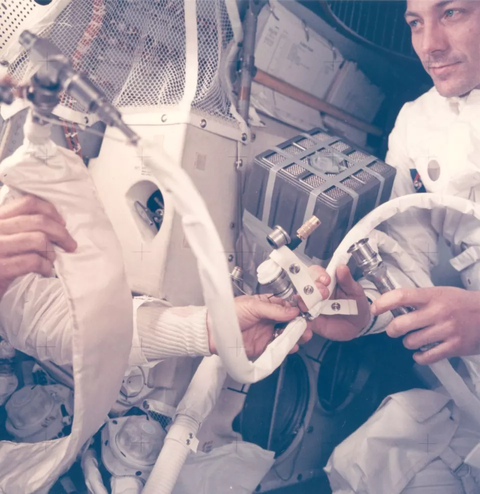 Dar bir kabinde, bantla tutturulmuş hortum ve kartuşlardan oluşan düzeneğin yanında duran astronot